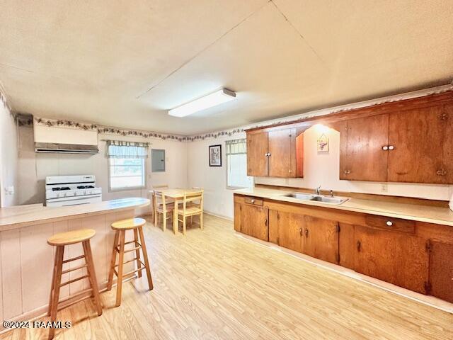 kitchen featuring stove, light hardwood / wood-style flooring, wall chimney range hood, sink, and a kitchen breakfast bar