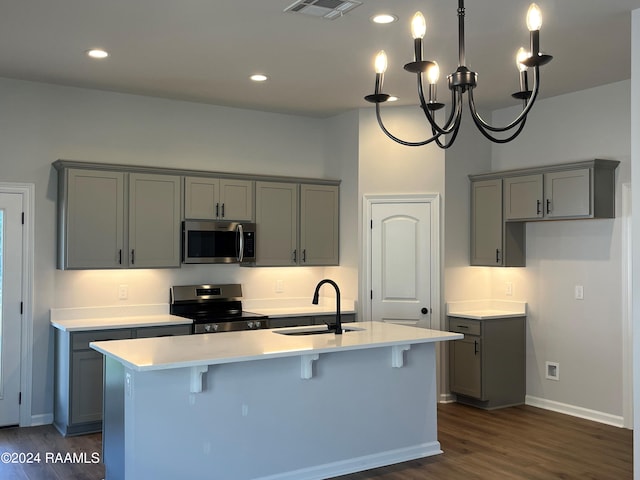 kitchen with sink, dark wood-type flooring, stainless steel appliances, an inviting chandelier, and an island with sink