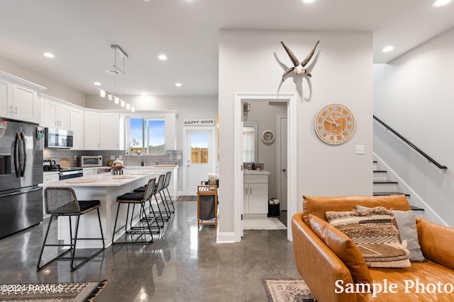 kitchen featuring appliances with stainless steel finishes, white cabinets, tasteful backsplash, a kitchen island, and a breakfast bar area