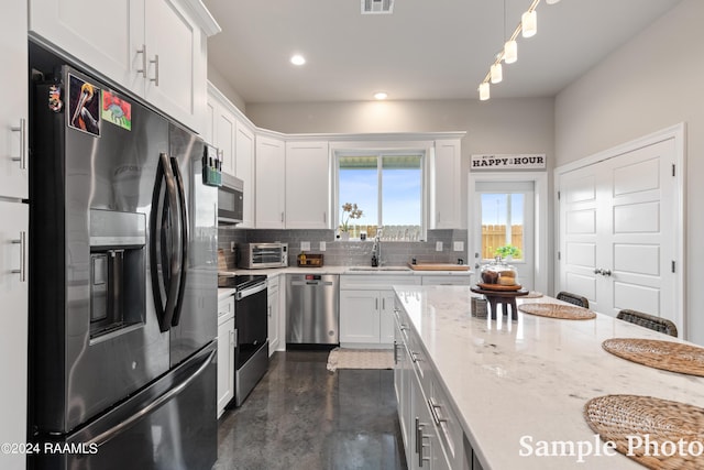 kitchen with light stone countertops, decorative light fixtures, white cabinetry, stainless steel appliances, and sink