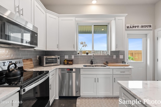 kitchen featuring appliances with stainless steel finishes, sink, white cabinetry, light stone counters, and decorative backsplash