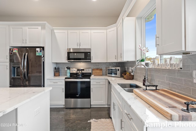 kitchen with appliances with stainless steel finishes, decorative backsplash, white cabinets, sink, and light stone counters