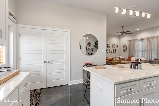 kitchen featuring decorative light fixtures, white cabinetry, light stone counters, a kitchen bar, and a center island