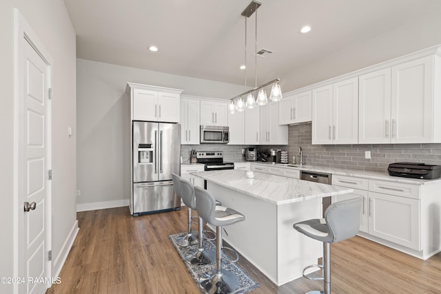 kitchen with a center island, hanging light fixtures, a breakfast bar area, stainless steel appliances, and white cabinets