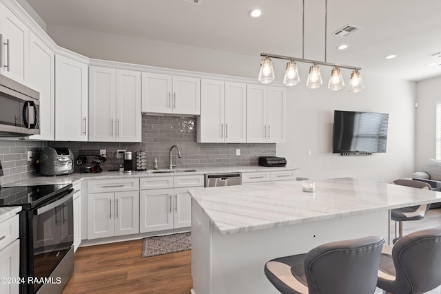 kitchen with appliances with stainless steel finishes, sink, white cabinetry, and a kitchen island