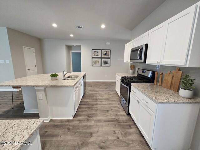 kitchen with light stone counters, stainless steel appliances, backsplash, hardwood / wood-style floors, and an island with sink