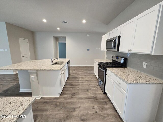 kitchen featuring light stone counters, stainless steel appliances, backsplash, an island with sink, and wood-type flooring