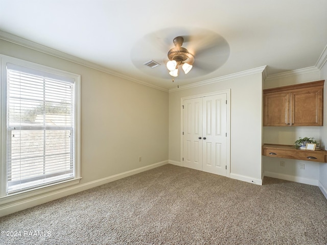 unfurnished bedroom featuring crown molding, ceiling fan, carpet, built in desk, and a closet