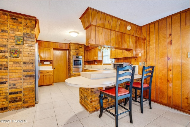 kitchen featuring light tile patterned floors, kitchen peninsula, a textured ceiling, and wooden walls