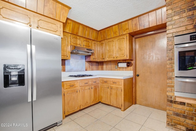 kitchen featuring light tile patterned flooring, appliances with stainless steel finishes, a textured ceiling, and wood walls