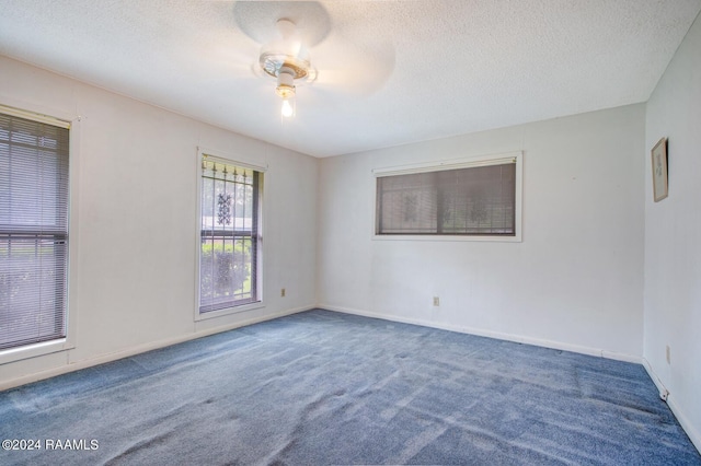 spare room featuring a textured ceiling, dark carpet, and ceiling fan