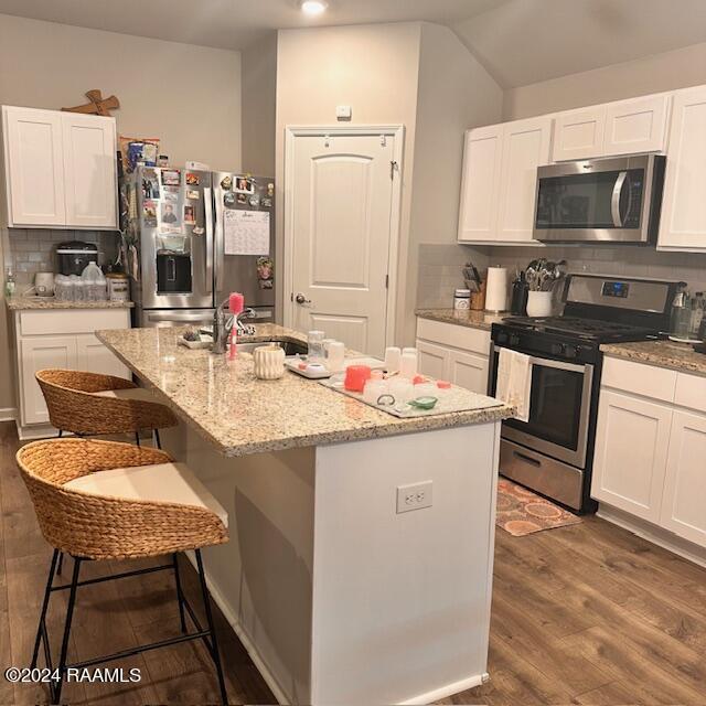 kitchen featuring white cabinetry, stainless steel appliances, backsplash, a breakfast bar area, and a kitchen island with sink