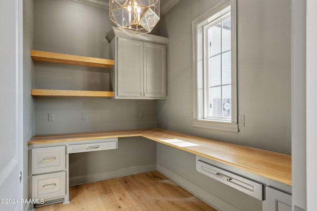 unfurnished office featuring crown molding, built in desk, and light hardwood / wood-style floors