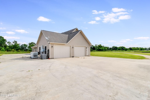 view of side of property featuring a garage, a yard, and central AC unit