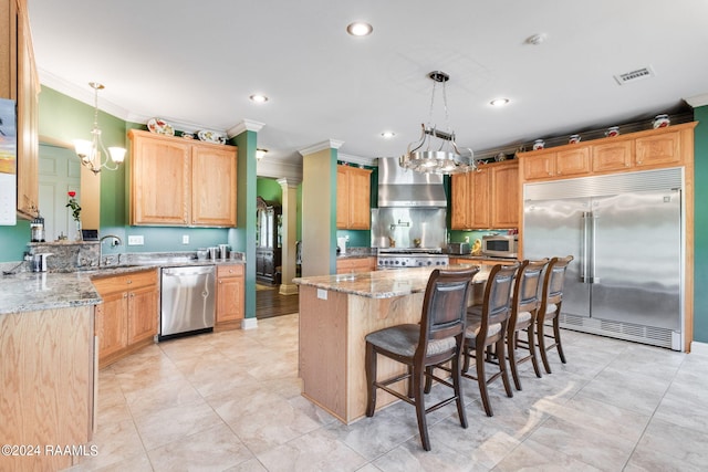 kitchen with wall chimney exhaust hood, sink, decorative light fixtures, a kitchen island, and stainless steel appliances