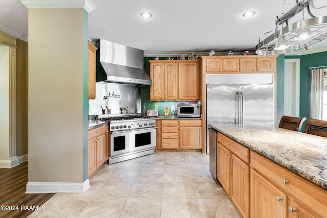 kitchen with appliances with stainless steel finishes, light tile patterned floors, crown molding, light stone countertops, and wall chimney exhaust hood