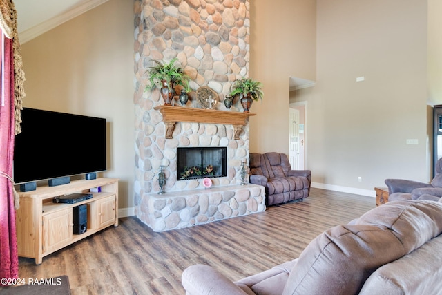 living room with hardwood / wood-style flooring, ornamental molding, a stone fireplace, and a high ceiling