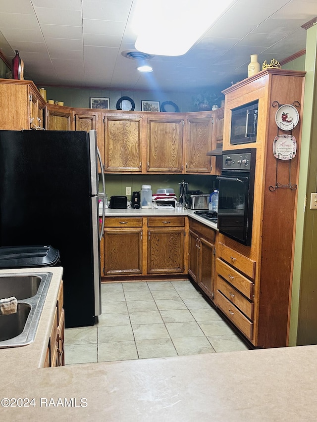 kitchen with brown cabinets, a sink, black appliances, light countertops, and light tile patterned flooring