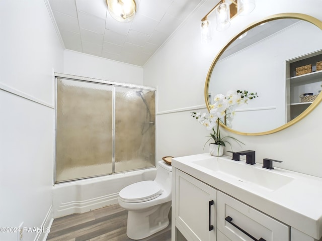 full bathroom featuring combined bath / shower with glass door, hardwood / wood-style floors, crown molding, toilet, and vanity