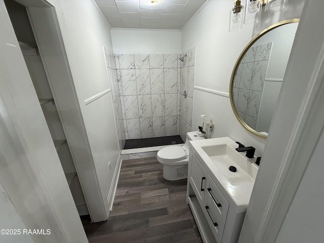 full bath featuring vanity, wood finished floors, tiled shower, crown molding, and toilet