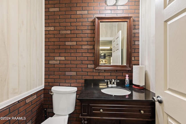 bathroom featuring toilet, brick wall, and vanity