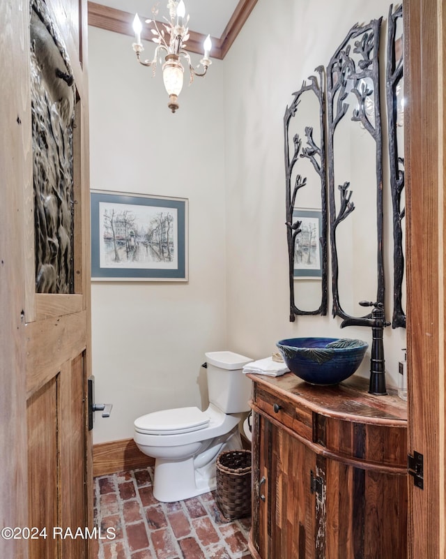 half bathroom featuring crown molding, toilet, vanity, brick floor, and a notable chandelier