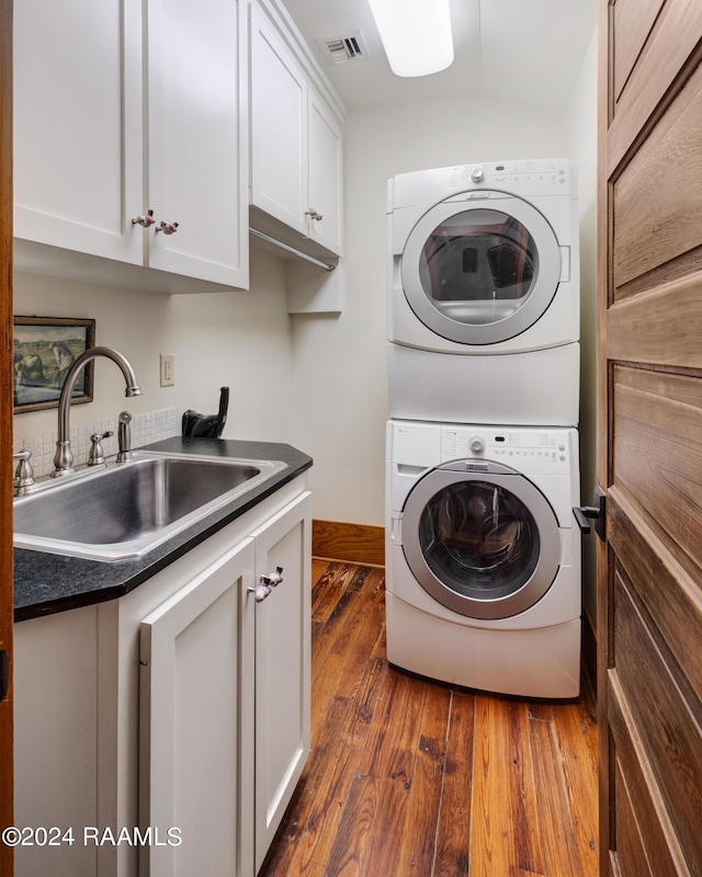 clothes washing area with dark wood-type flooring, stacked washer and dryer, a sink, visible vents, and cabinet space