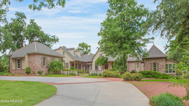 view of front of house featuring brick siding, fence, curved driveway, and a front yard