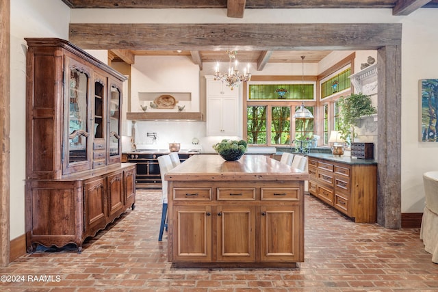 kitchen with an inviting chandelier, brick floor, beamed ceiling, and brown cabinets
