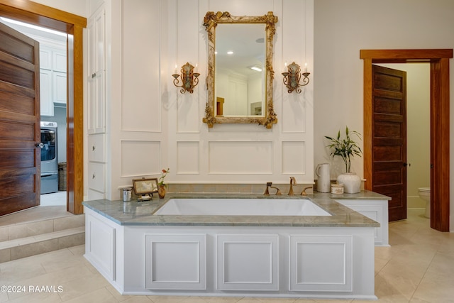 bathroom with a decorative wall, toilet, tile patterned flooring, and washer / dryer