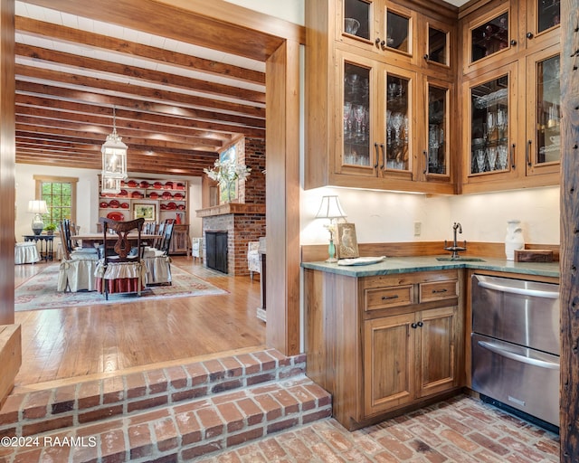 kitchen featuring a sink, beam ceiling, brick floor, brown cabinetry, and glass insert cabinets