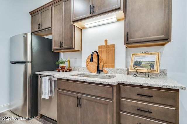 kitchen featuring light stone counters, light hardwood / wood-style floors, stainless steel appliances, and sink