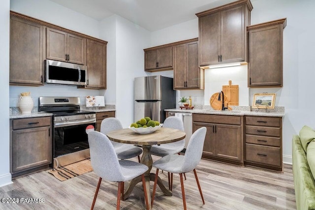 kitchen with light hardwood / wood-style floors, appliances with stainless steel finishes, sink, and light stone counters