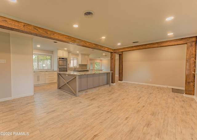 kitchen with white cabinetry, light hardwood / wood-style flooring, stainless steel double oven, a large island, and light stone countertops