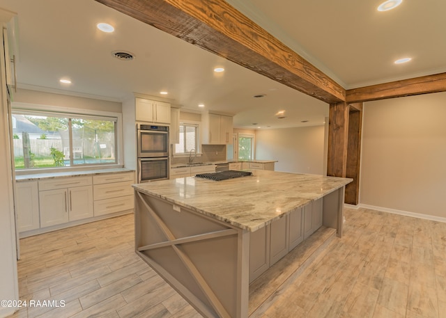 kitchen with sink, white cabinetry, a center island, light stone counters, and stainless steel double oven