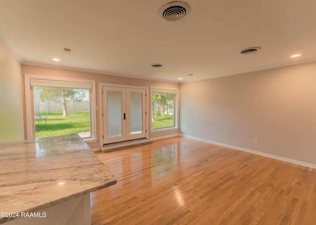 unfurnished living room featuring crown molding, french doors, and light wood-type flooring