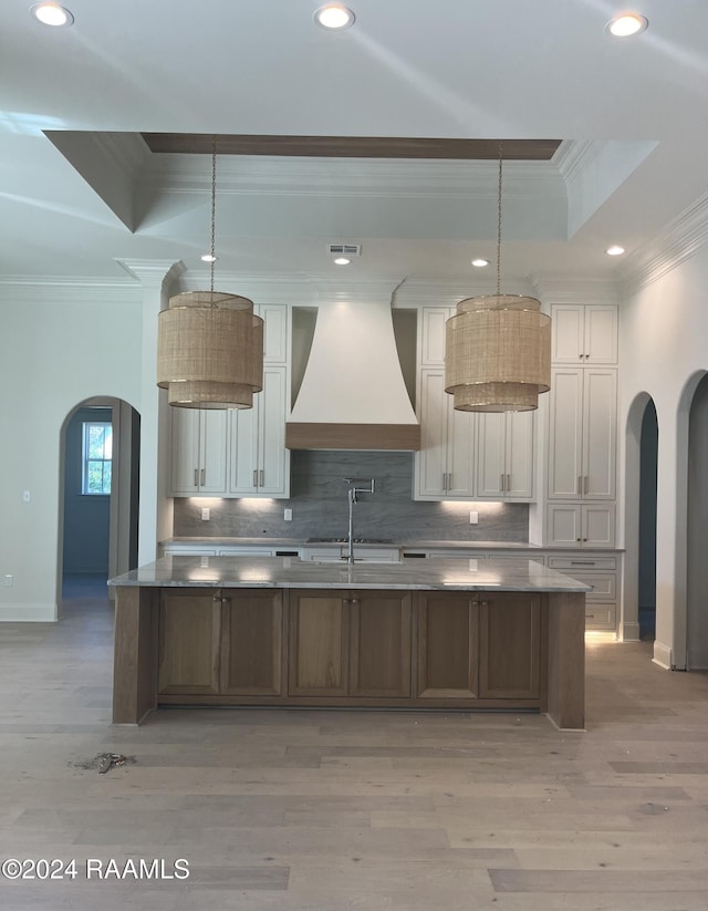 kitchen with custom exhaust hood, decorative light fixtures, light hardwood / wood-style floors, a tray ceiling, and white cabinets