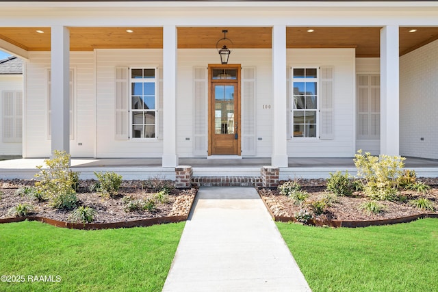 view of exterior entry featuring a porch and a lawn