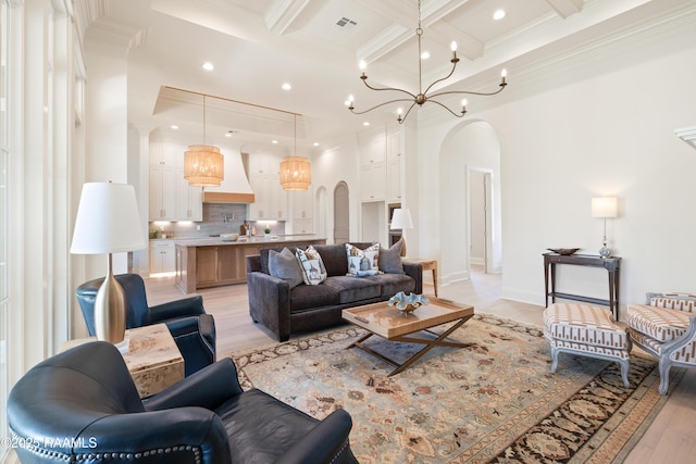 living room with arched walkways, a notable chandelier, ornamental molding, coffered ceiling, and beamed ceiling