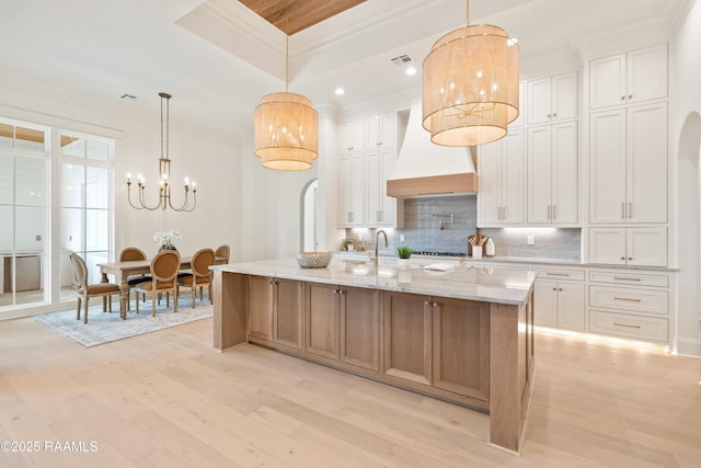 kitchen featuring light wood-style flooring, white cabinets, ornamental molding, a large island, and decorative backsplash