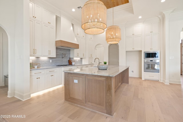 kitchen with light wood-type flooring, custom range hood, appliances with stainless steel finishes, and arched walkways