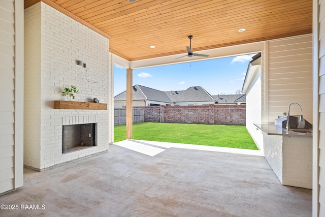 view of patio featuring ceiling fan, an outdoor brick fireplace, fence, and an outdoor kitchen