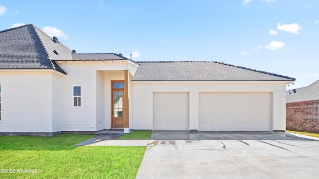 view of front of property featuring concrete driveway, a front lawn, roof with shingles, and an attached garage