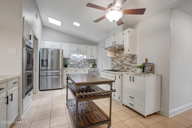 kitchen with lofted ceiling with skylight, light tile patterned flooring, tasteful backsplash, white cabinets, and stainless steel appliances