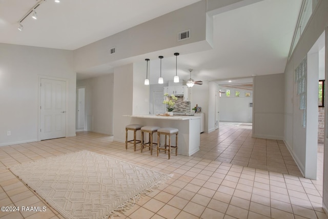 kitchen with white cabinets, a kitchen bar, decorative backsplash, hanging light fixtures, and light tile patterned floors