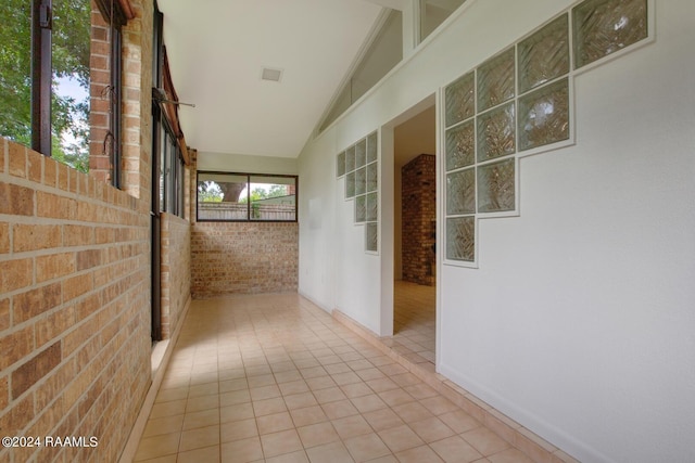 hallway with vaulted ceiling, brick wall, and light tile patterned floors