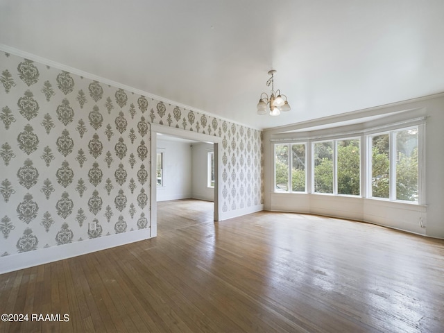 empty room with ornamental molding, hardwood / wood-style flooring, and a notable chandelier