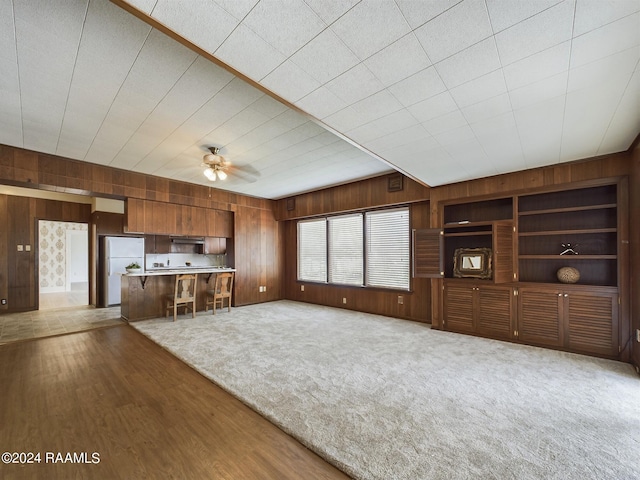 unfurnished living room featuring hardwood / wood-style flooring, built in features, wooden walls, and ceiling fan