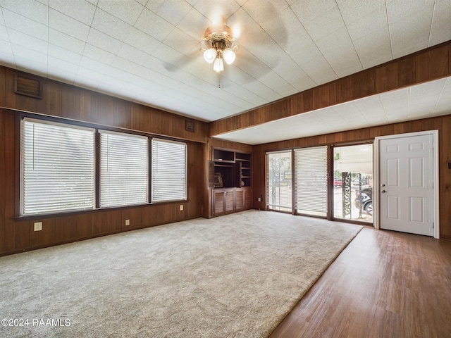 unfurnished living room with wooden walls, built in features, hardwood / wood-style floors, and ceiling fan