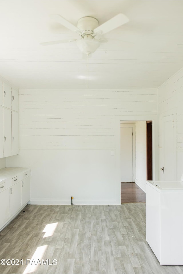 unfurnished room with washer / clothes dryer, ceiling fan, light hardwood / wood-style floors, and wood walls